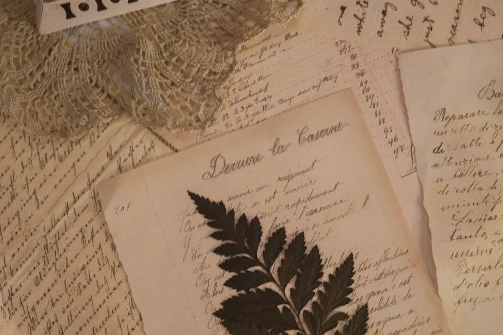 Lettres manuscrites jaunies, fougère séchée et petite flamme sur une table